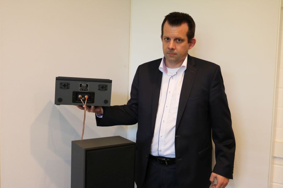Voxx German Holdings International Sales Manager Mario Lode holding a Cinema Ulta AEH 400-ATM Atmos speaker which can be placed on top of hte front speakers or on the ceiling.