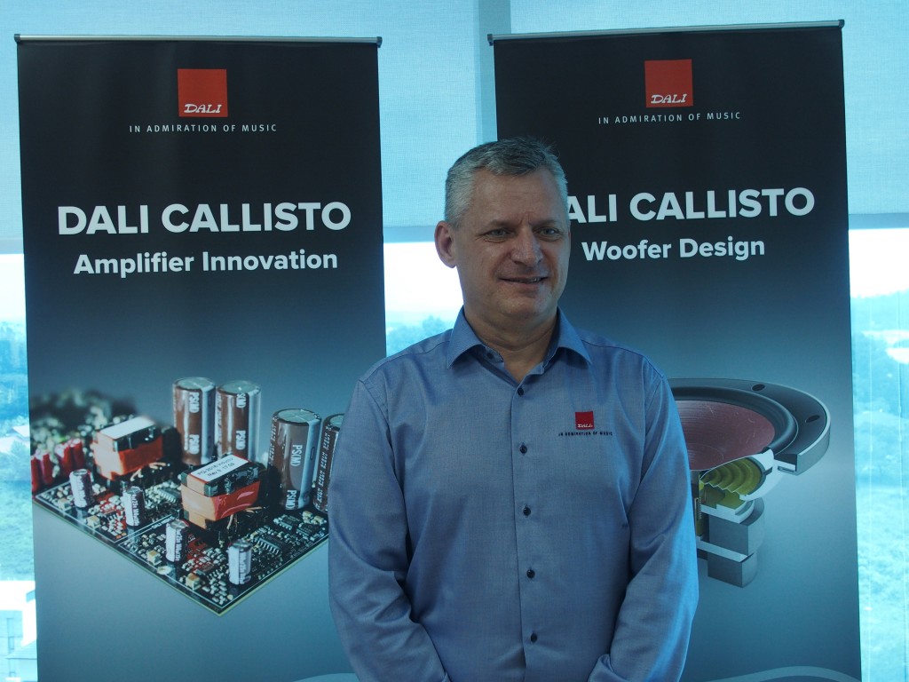 Michael Pederson posing in front of banners showing the technologies used in the Callisto system.